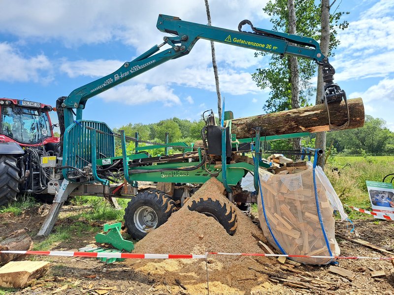 Traktor mit Anhänger, auf dem ein Spalter montiert ist.